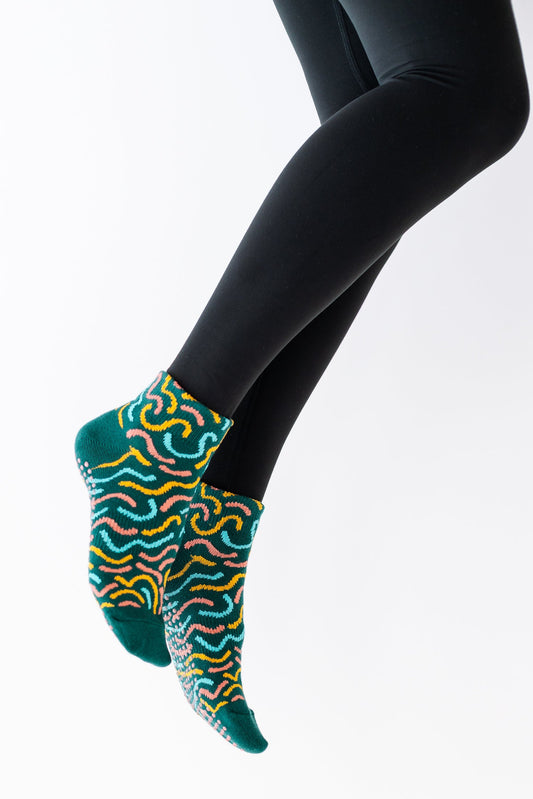 A pair of colorful 'Groovy Grip' ankle socks worn on legs against a white background, showcasing a geometric pattern in multicolored hues.